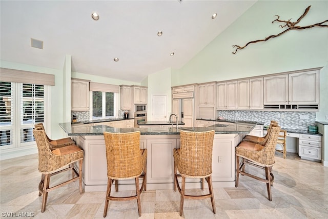 kitchen featuring a kitchen bar, built in appliances, plenty of natural light, and a kitchen island with sink