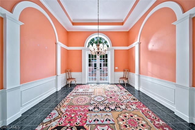 interior space with french doors, dark tile flooring, a raised ceiling, decorative columns, and an inviting chandelier