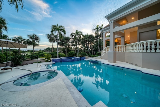 pool at dusk featuring an in ground hot tub