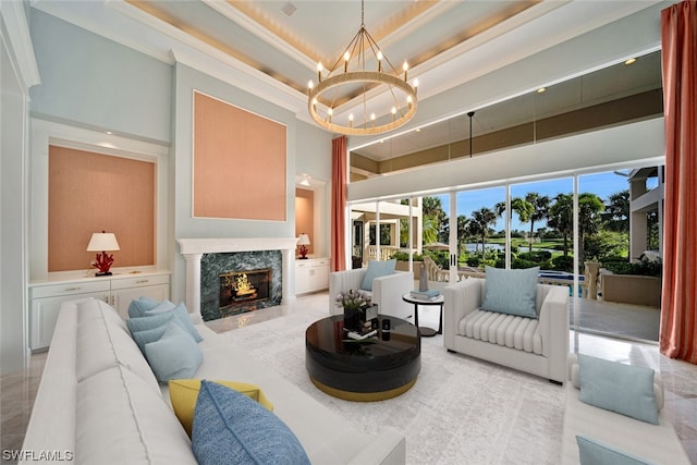 living room featuring a towering ceiling, a raised ceiling, ornamental molding, a fireplace, and a notable chandelier