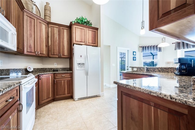 kitchen featuring light tile floors, a high ceiling, white appliances, hanging light fixtures, and dark stone countertops