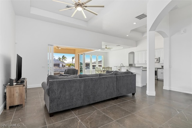 tiled living room with ceiling fan, a raised ceiling, and a high ceiling