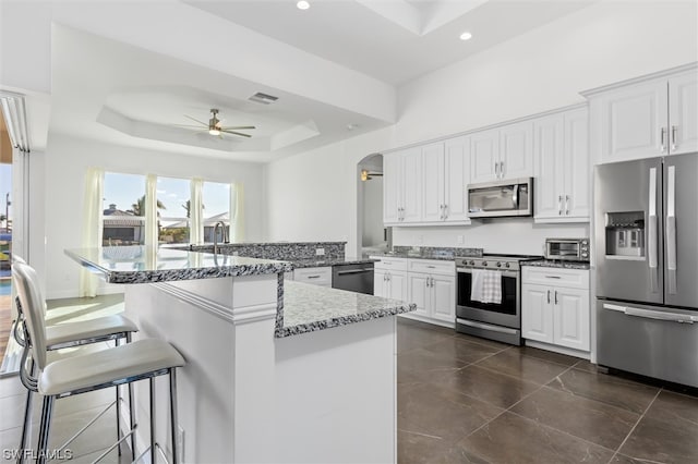 kitchen featuring dark tile floors, white cabinets, stainless steel appliances, a raised ceiling, and ceiling fan