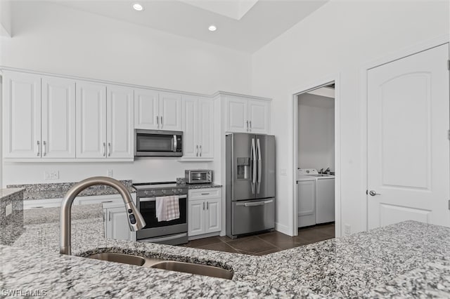 kitchen featuring light stone counters, appliances with stainless steel finishes, dark tile floors, washing machine and clothes dryer, and white cabinetry