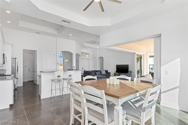 dining area with ceiling fan, dark tile floors, a wealth of natural light, and a tray ceiling