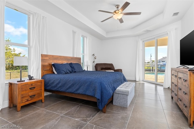 tiled bedroom featuring multiple windows, ceiling fan, access to exterior, and a tray ceiling