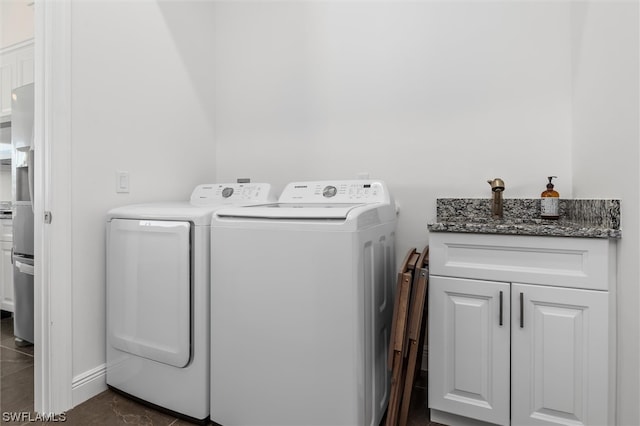 clothes washing area featuring cabinets, washer and clothes dryer, and dark tile floors