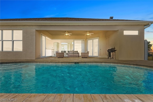 pool at dusk featuring outdoor lounge area, ceiling fan, and a patio