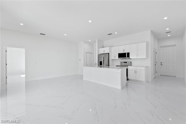 kitchen with appliances with stainless steel finishes, a center island, light tile patterned flooring, and white cabinets