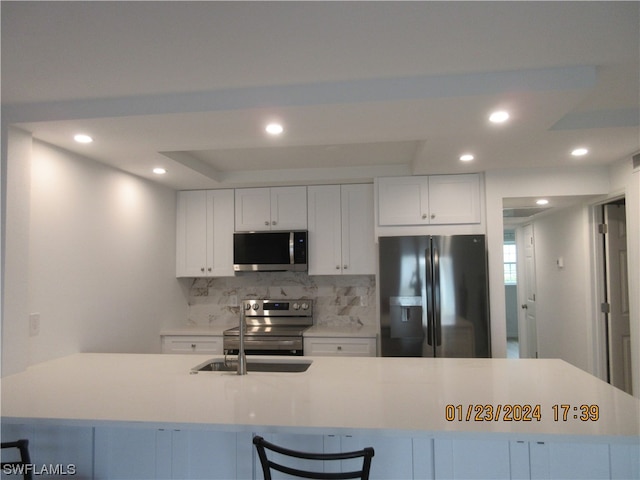 kitchen with stainless steel appliances, white cabinets, backsplash, a tray ceiling, and sink