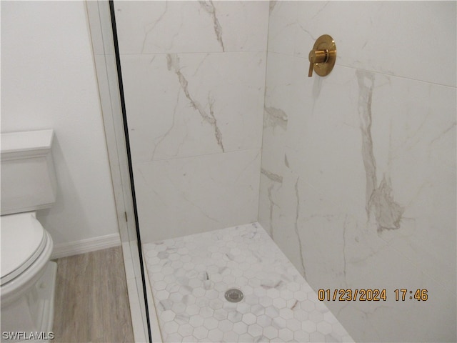 bathroom with toilet, tiled shower, and hardwood / wood-style flooring