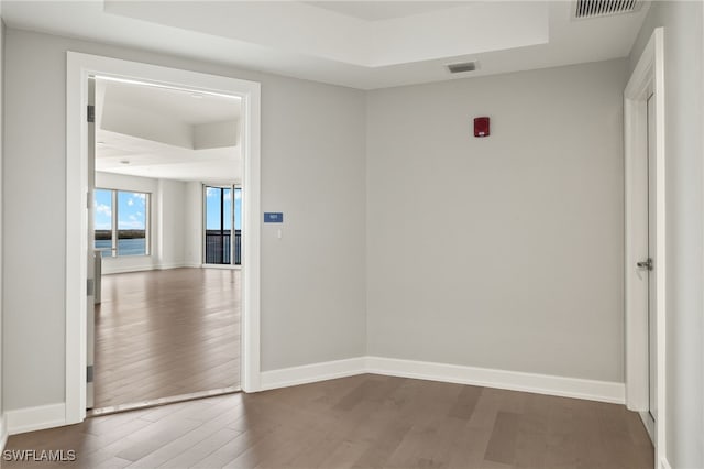 empty room with a tray ceiling, wood finished floors, visible vents, and baseboards