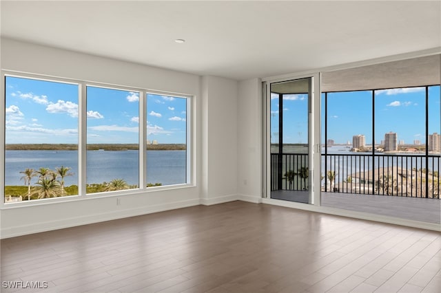 empty room featuring a water view, wood finished floors, and baseboards