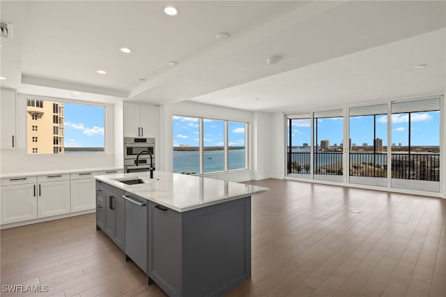 kitchen with light wood finished floors, recessed lighting, gray cabinets, stainless steel double oven, and a sink