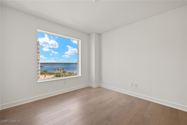 empty room with a water view, baseboards, and wood finished floors