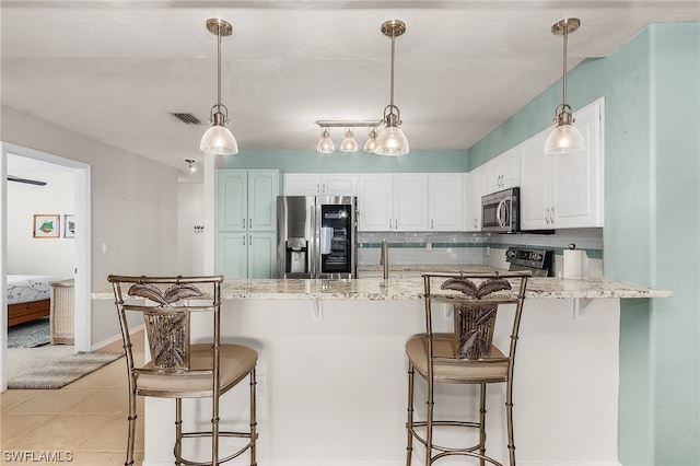 kitchen featuring light tile floors, light stone countertops, appliances with stainless steel finishes, white cabinetry, and hanging light fixtures