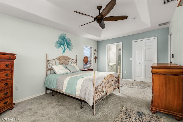 bedroom with ensuite bath, ceiling fan, a closet, light carpet, and a tray ceiling