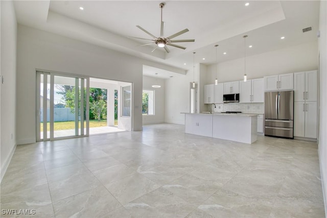 kitchen with a high ceiling, white cabinets, a raised ceiling, hanging light fixtures, and stainless steel appliances