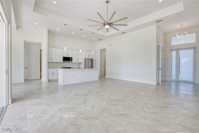 unfurnished living room featuring a high ceiling, ceiling fan with notable chandelier, and a raised ceiling