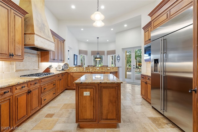 kitchen featuring built in appliances, a center island, pendant lighting, and custom range hood