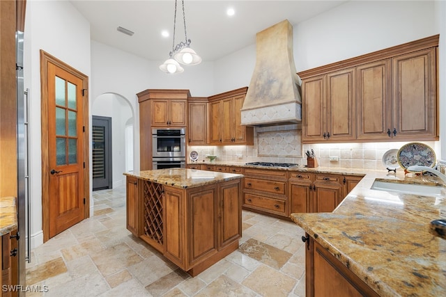 kitchen with custom exhaust hood, stainless steel appliances, sink, a center island, and hanging light fixtures