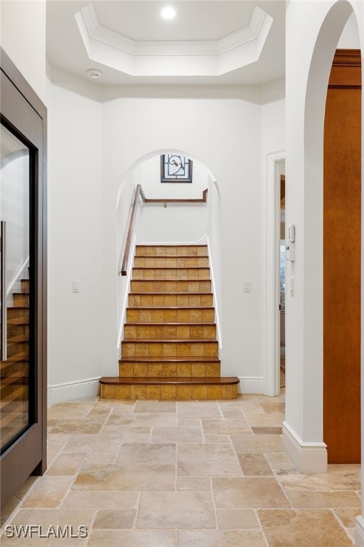 staircase featuring a raised ceiling and crown molding