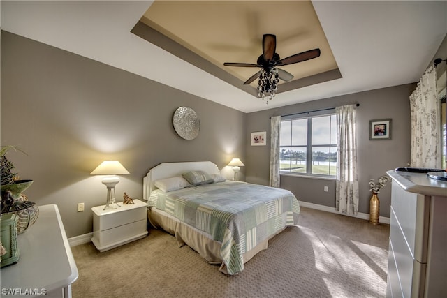 bedroom featuring light carpet, ceiling fan, and a tray ceiling