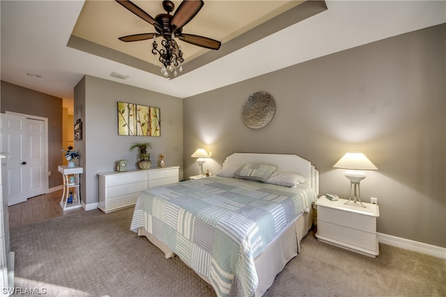 bedroom with light carpet, ceiling fan, and a tray ceiling