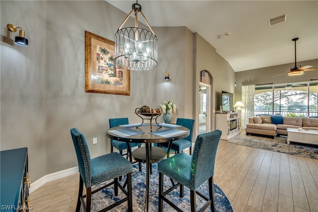 dining space with high vaulted ceiling, ceiling fan with notable chandelier, and light wood-type flooring