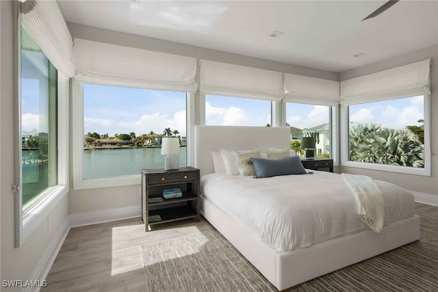 bedroom featuring wood-type flooring, multiple windows, and a water view