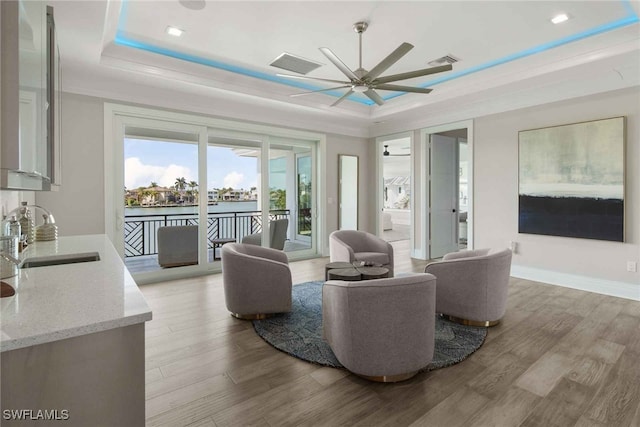 living room with ceiling fan, a raised ceiling, sink, and light hardwood / wood-style flooring