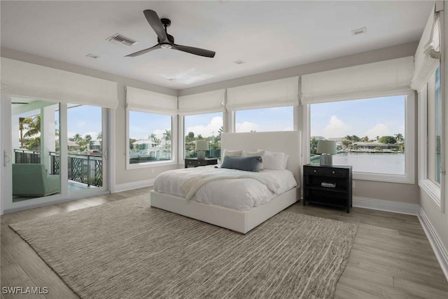 bedroom featuring a water view, access to exterior, light hardwood / wood-style flooring, and ceiling fan