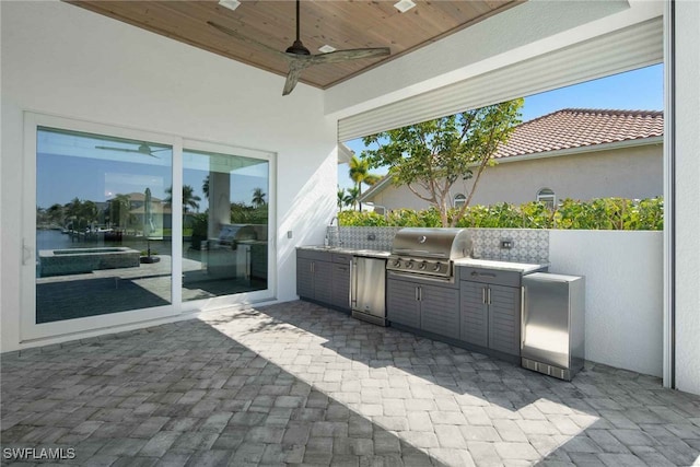 view of patio with ceiling fan, a grill, a water view, and exterior kitchen