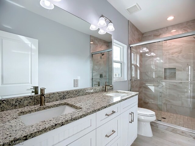 bathroom featuring an enclosed shower, toilet, and dual vanity