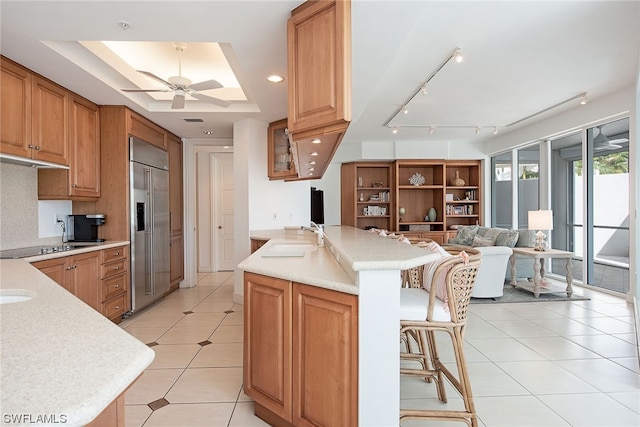 kitchen featuring ceiling fan, a breakfast bar, sink, a raised ceiling, and stainless steel built in refrigerator