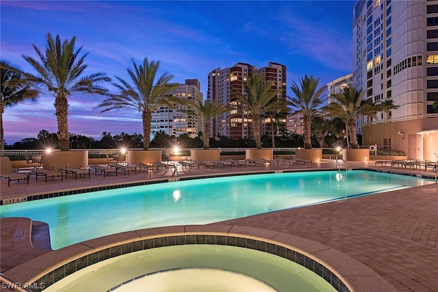 pool at dusk featuring a hot tub