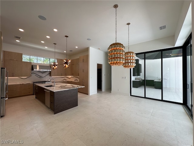 kitchen featuring light stone counters, light tile patterned flooring, pendant lighting, a center island with sink, and tasteful backsplash