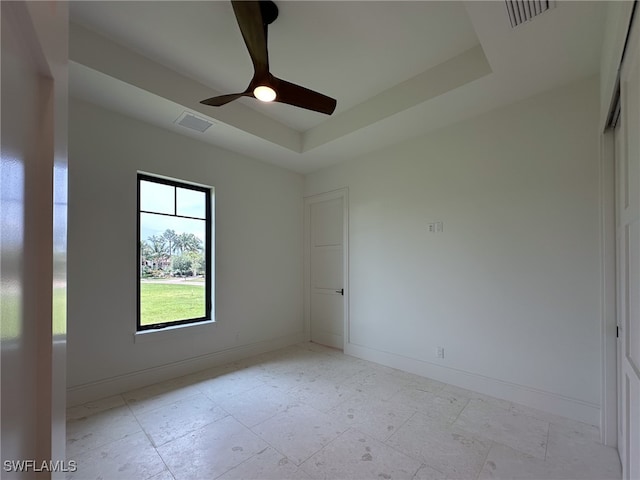 spare room featuring a raised ceiling, ceiling fan, and light tile patterned floors