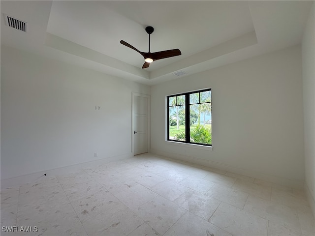 unfurnished room with a raised ceiling, ceiling fan, and light tile patterned flooring