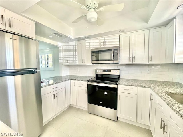 kitchen with white cabinets, light stone countertops, appliances with stainless steel finishes, and a tray ceiling