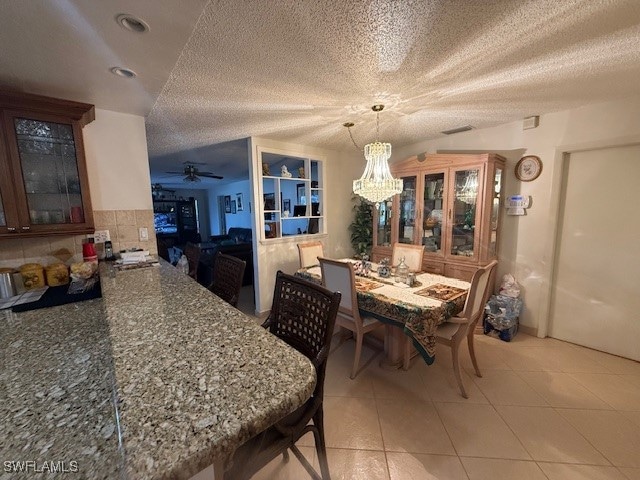 dining room featuring ceiling fan with notable chandelier, light tile patterned floors, and a textured ceiling