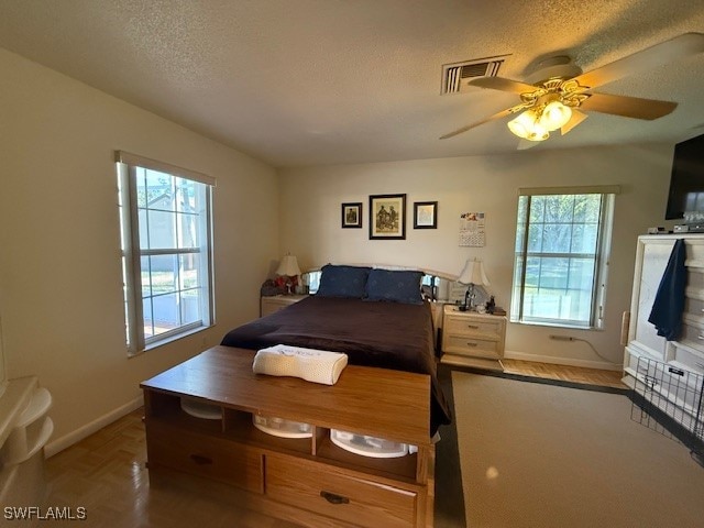 bedroom featuring multiple windows, a textured ceiling, parquet floors, and ceiling fan