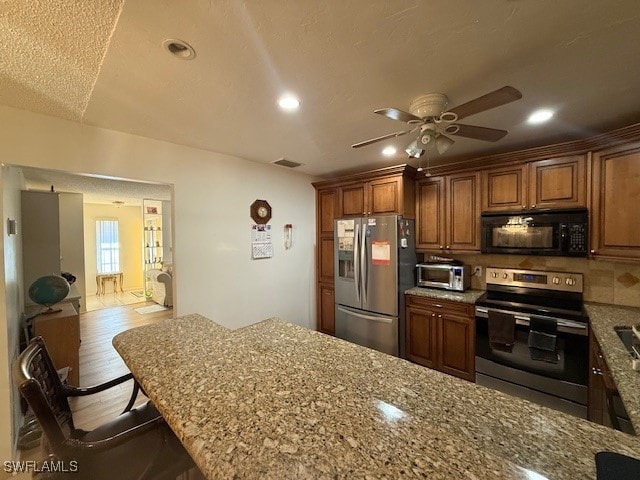 kitchen featuring a kitchen breakfast bar, stainless steel appliances, light hardwood / wood-style flooring, and light stone counters