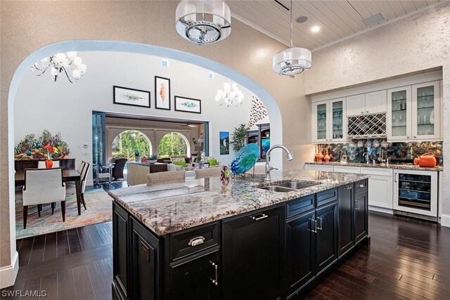 kitchen featuring sink, beverage cooler, a kitchen island with sink, a chandelier, and white cabinetry