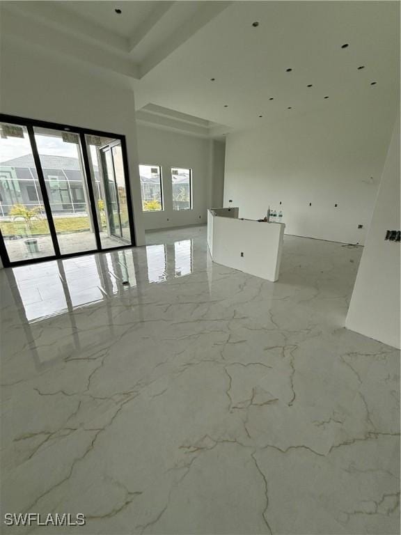 spare room with a wealth of natural light, marble finish floor, and a high ceiling