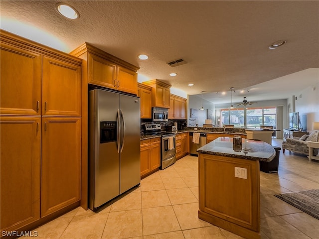 kitchen featuring kitchen peninsula, ceiling fan, appliances with stainless steel finishes, dark stone countertops, and light tile floors