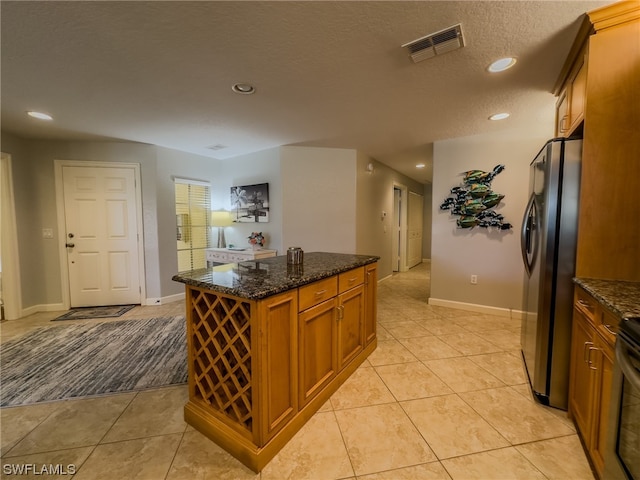 kitchen with light tile floors, dark stone counters, a textured ceiling, and stainless steel refrigerator