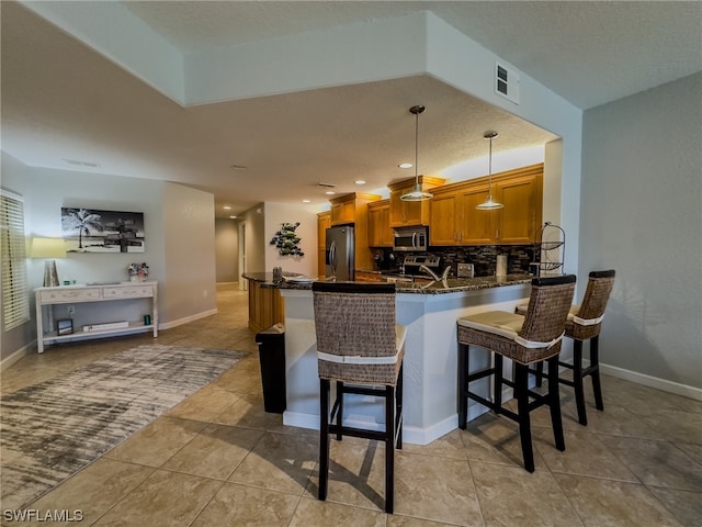 kitchen with pendant lighting, stainless steel appliances, kitchen peninsula, tasteful backsplash, and a breakfast bar area