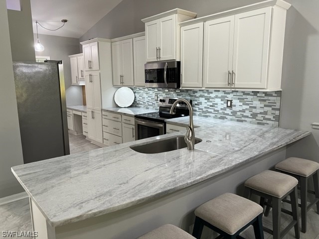 kitchen with kitchen peninsula, a kitchen breakfast bar, stainless steel appliances, vaulted ceiling, and tasteful backsplash