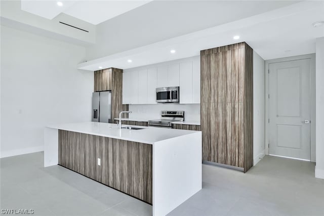 kitchen with stainless steel appliances, light tile flooring, a center island with sink, white cabinets, and sink